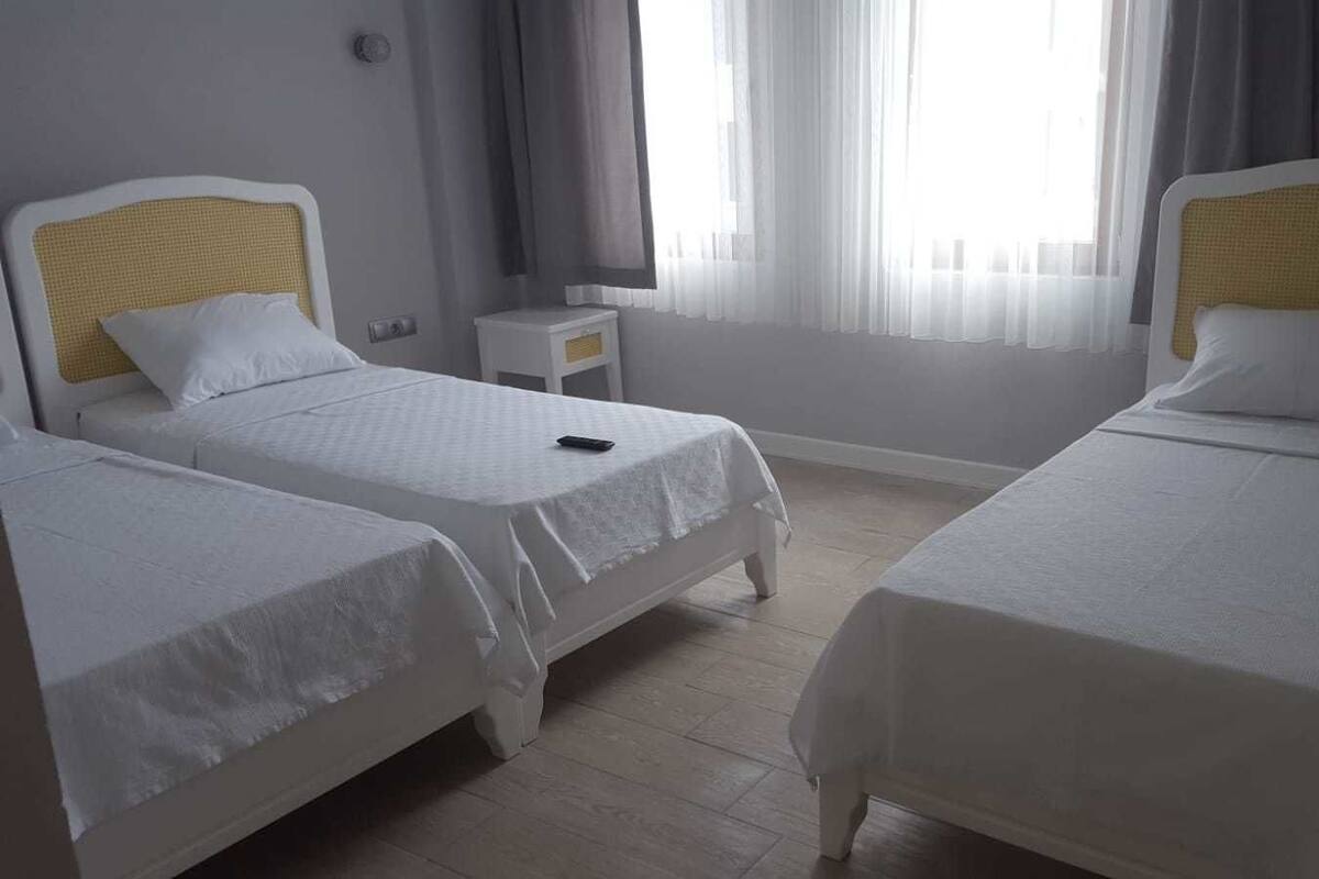 A hotel room with two single beds, a small bedside table, and a window with sheer curtains.