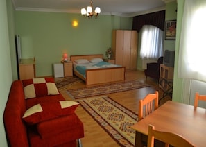Una habitación con una cama, un sofá rojo, una mesa de madera y un televisor.
