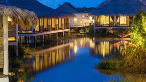 A resort with thatched-roof structures, a water body, and a wooden deck. - Sripakpra Boutique Resort Phatthalung (Khuan Khanun)