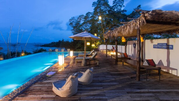 A wooden deck with lounge chairs and bean bags by a pool, a thatched roof structure, and a sign indicating a location. - Sripakpra Boutique Resort Phatthalung (Khuan Khanun)