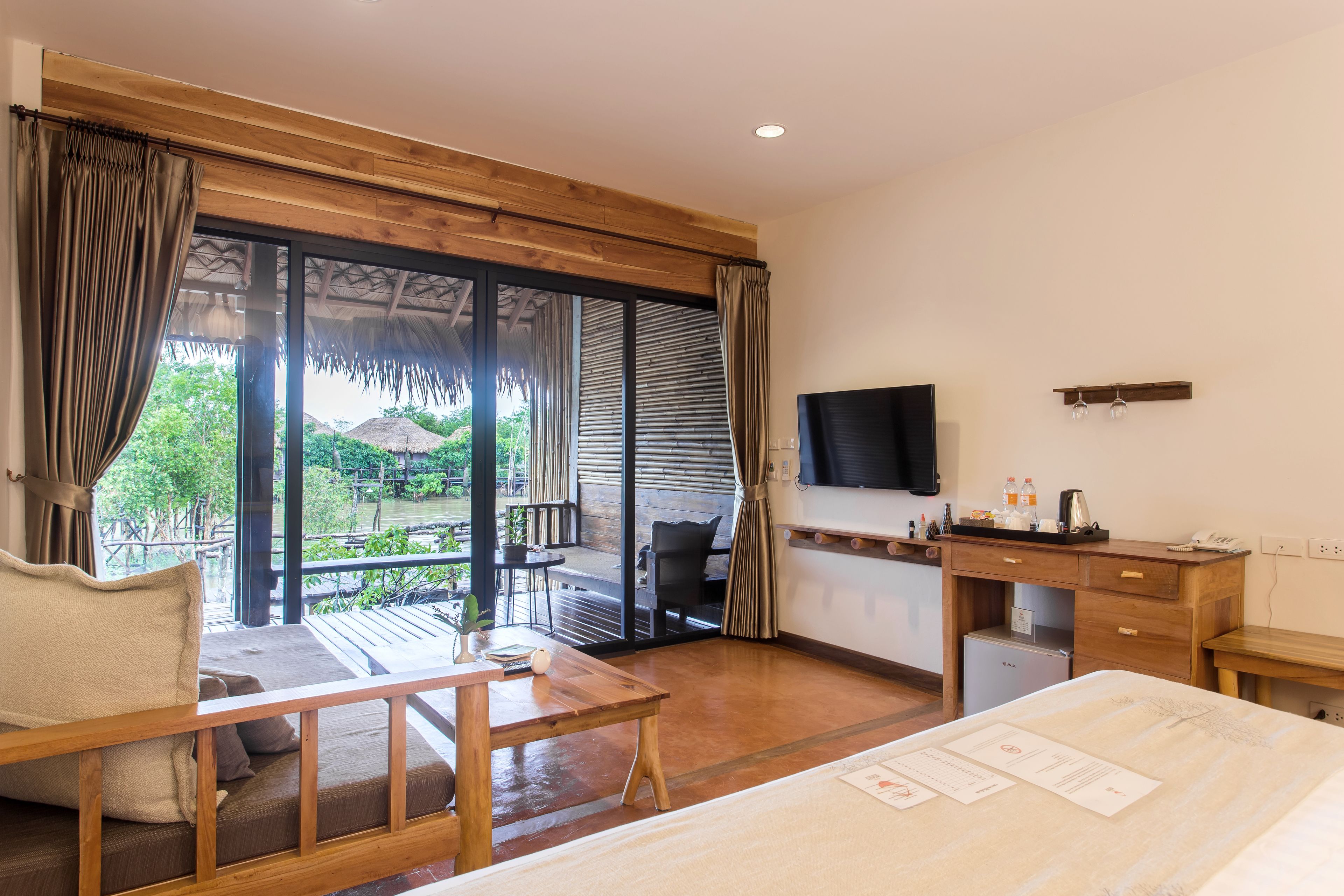 Habitación de hotel con escritorio de madera, cama, televisor y balcón con vistas a zonas verdes.