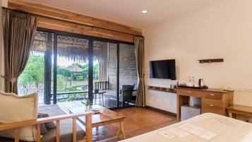 Habitación de hotel con escritorio de madera, cama, televisor y balcón con vistas a zonas verdes.