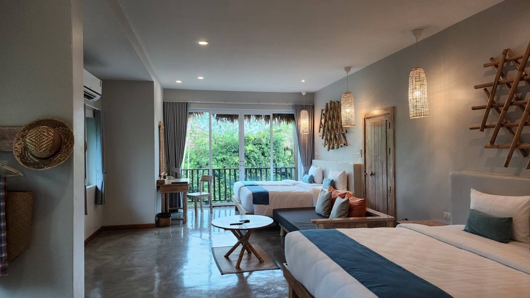A hotel room with a large bed, a desk, and a balcony with a view of greenery.