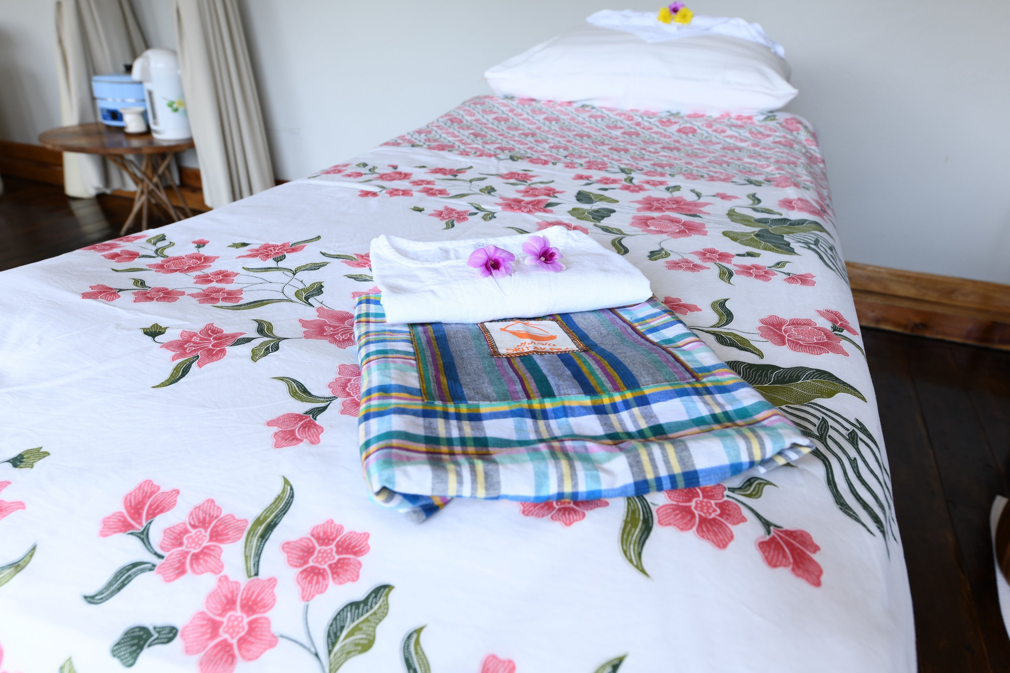 Ein ordentlich bezogenes Bett mit floralem Bettwäsche, ein gefaltetes Handtuch und ein gestreiftes Kissen.