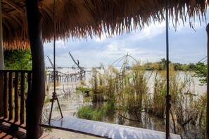 A wooden deck with a thatched roof overlooking a water body with fishing nets. - Sripakpra Boutique Resort Phatthalung (Khuan Khanun)