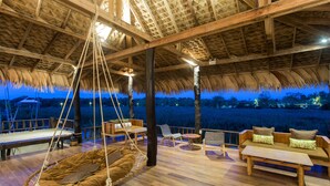 An outdoor wooden deck with a thatched roof, hanging chairs, and a sofa area with cushions. - Sripakpra Boutique Resort Phatthalung (Khuan Khanun)