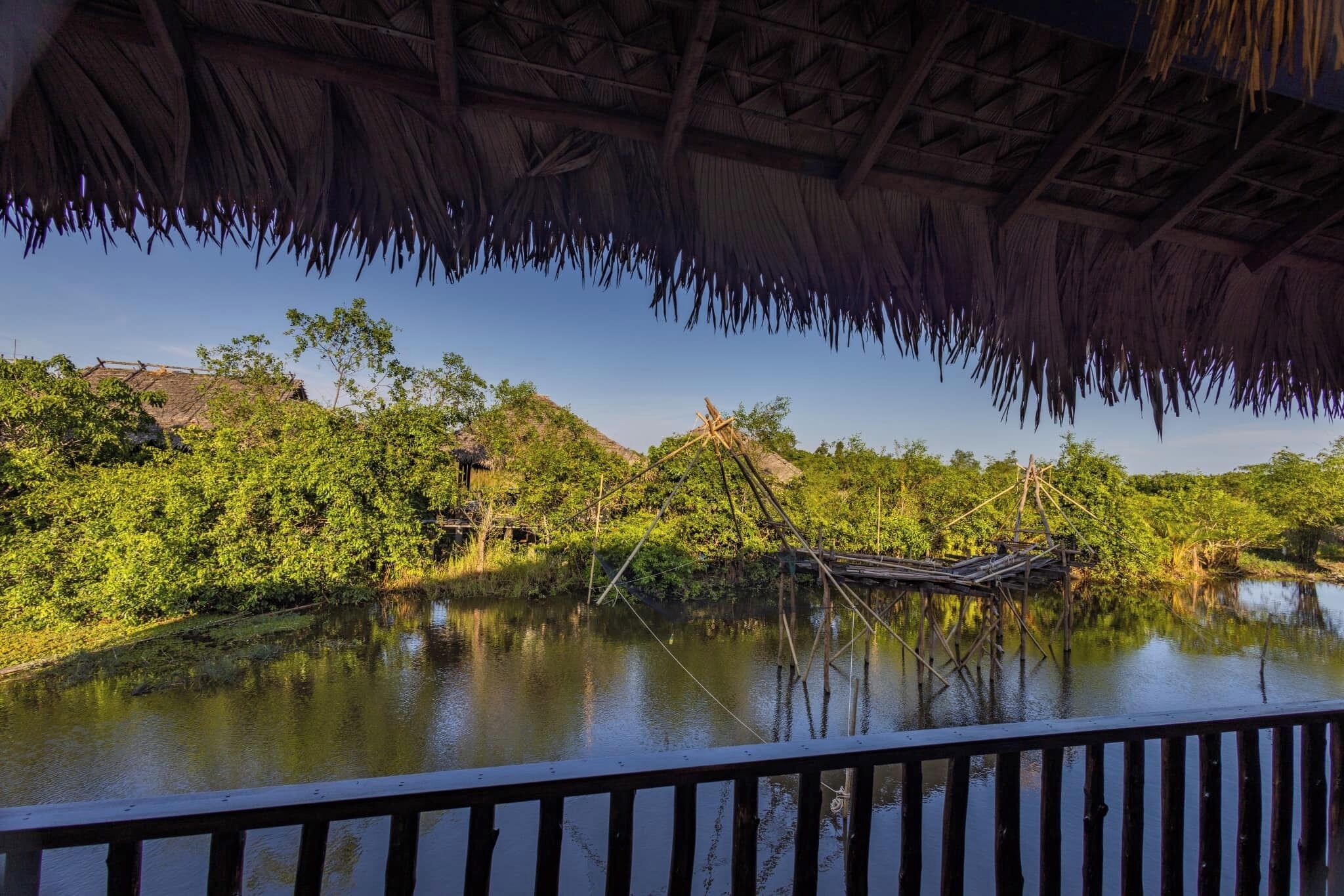 A thatched-roof structure with a view of a river and surrounding greenery.