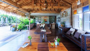 A spacious indoor area with a wooden ceiling, a long dining table, and a seating area with cushions. - Sripakpra Boutique Resort Phatthalung (Khuan Khanun)