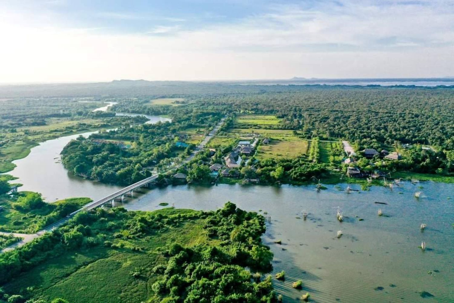 A river with a bridge, surrounded by greenery and small buildings.