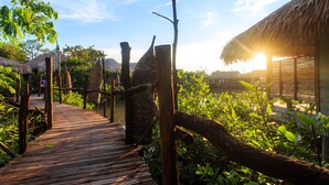 A wooden pathway leading to a thatched-roof structure surrounded by lush greenery. - Sripakpra Boutique Resort Phatthalung (Khuan Khanun)