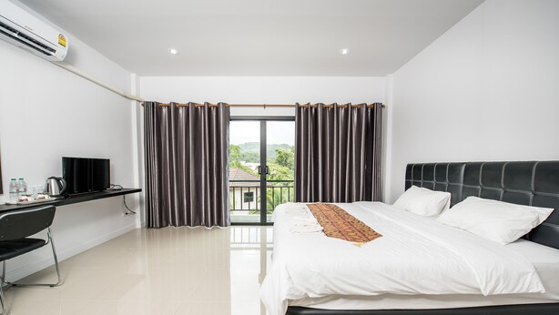 A modern hotel room with a large bed, a desk, and a view of greenery through the window. - Mr. T Kamala Room (Kamala)