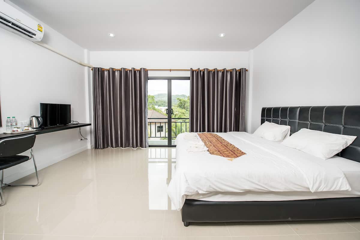 A modern hotel room with a large bed, a desk, and a view of greenery through the window.