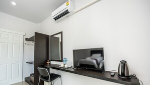 A modern hotel room with a flat-screen TV, a kettle, a small table with water bottles, a chair, and a large mirror. - Mr. T Kamala Room (Kamala)