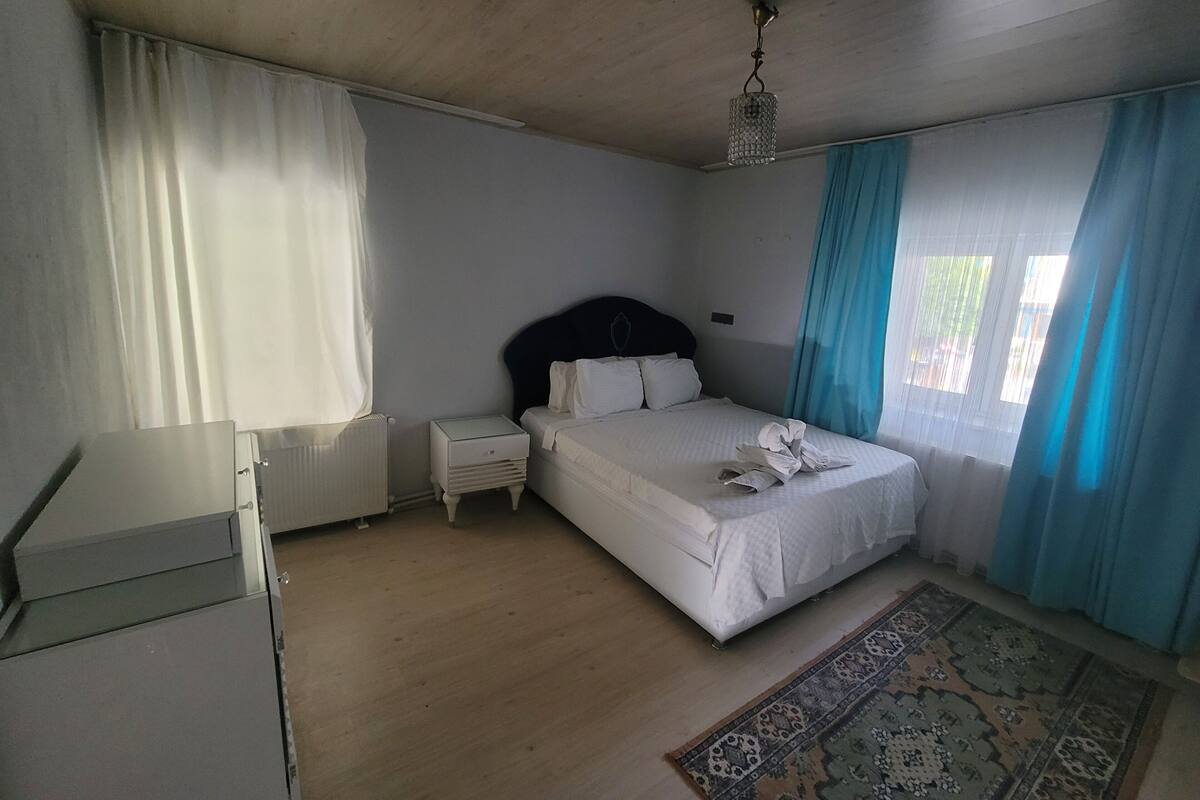 Un dormitorio con cama, mesitas de noche, un radiador y una lámpara en el techo.