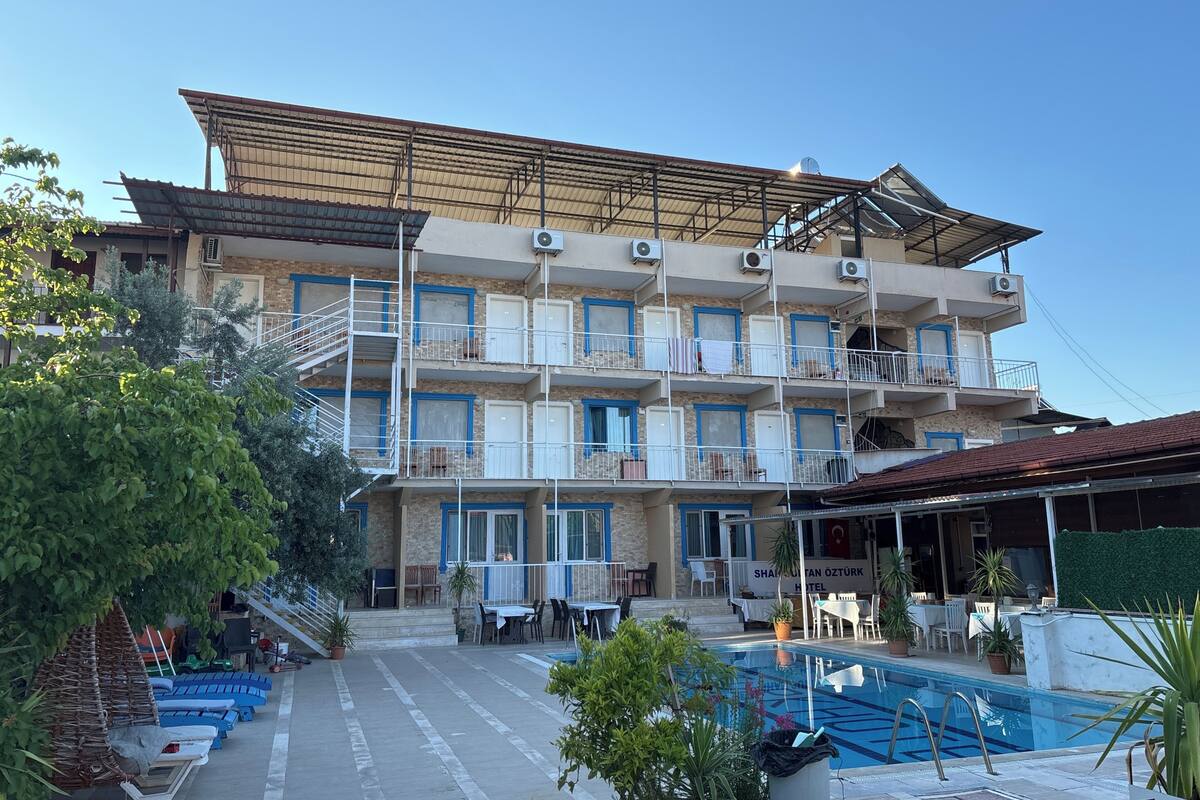 Un hotel de varios pisos con balcones, piscina y mobiliario exterior.