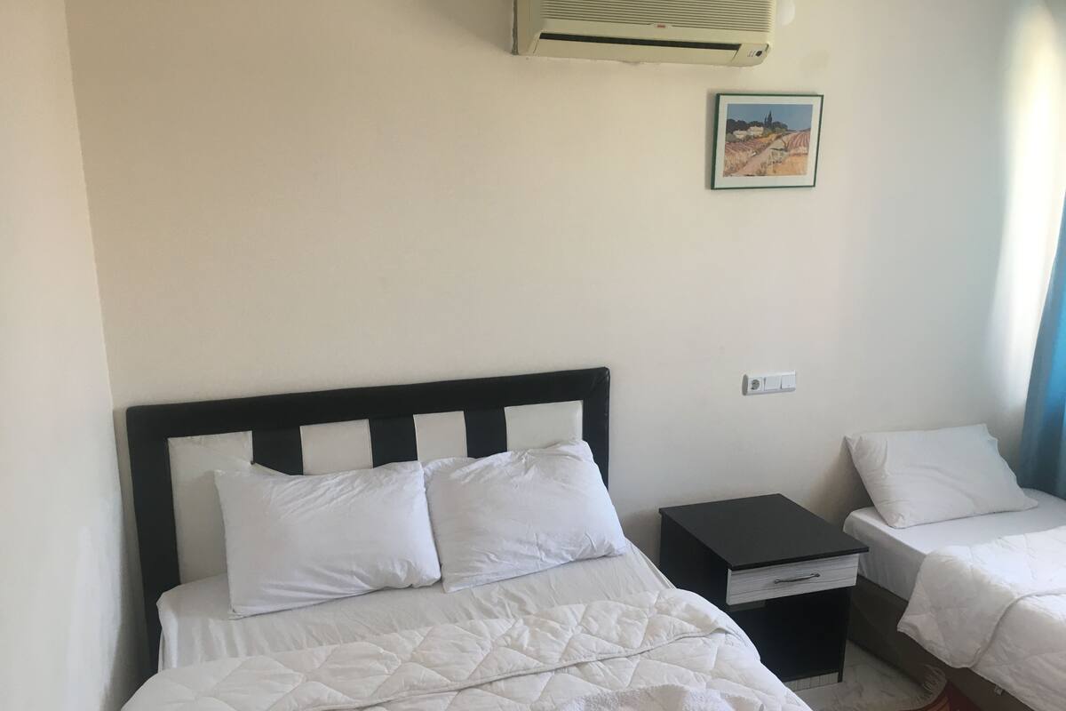 Una habitación de hotel con una cama grande, una cama más pequeña, una mesita de noche y un aire acondicionado de pared.