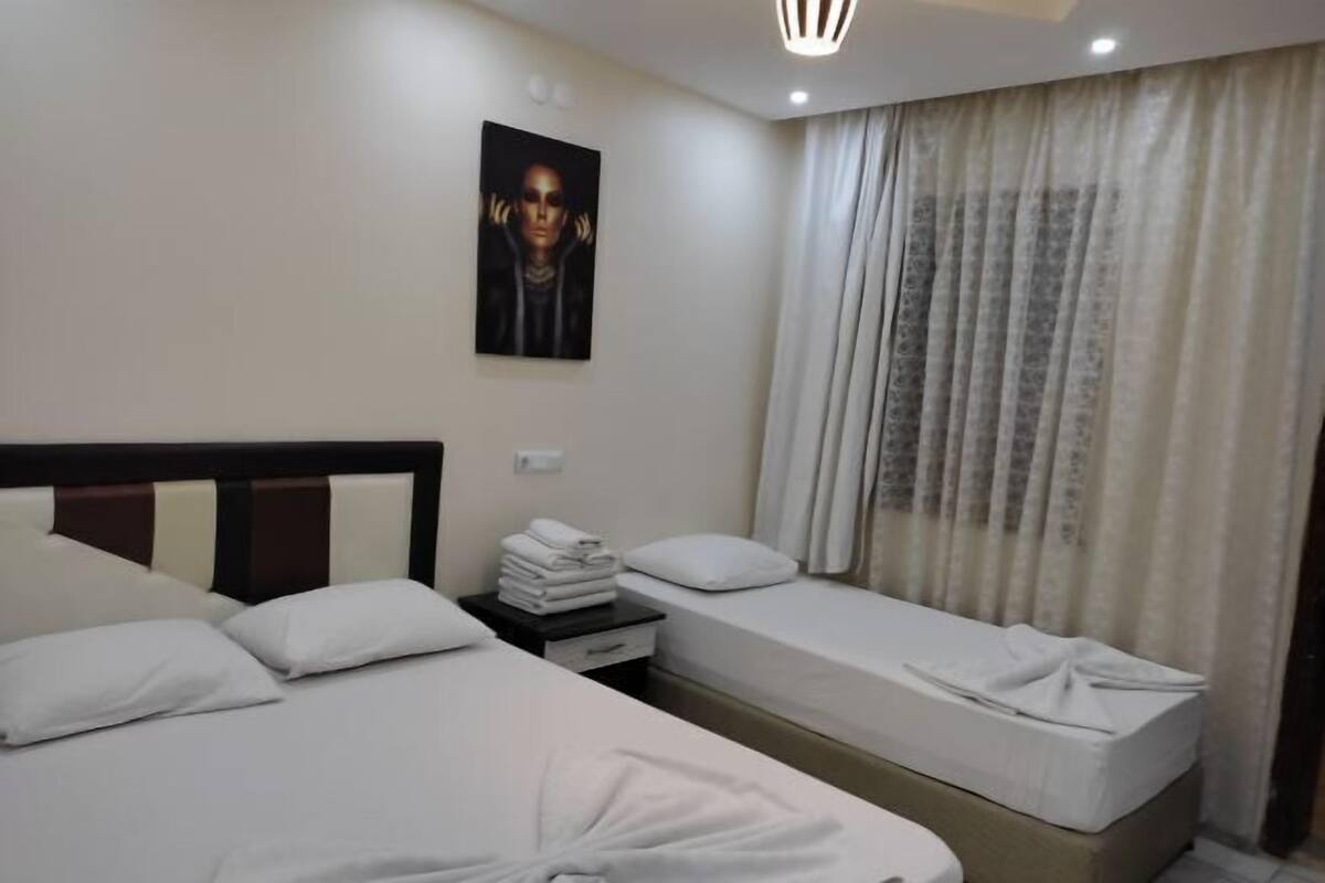 Habitación de hotel con dos camas, una mesita de noche con toallas, un cuadro en la pared y una ventana con cortinas.