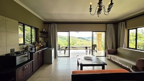 A spacious living area with a kitchen, a dining table, a sofa, and a view of the outdoors.