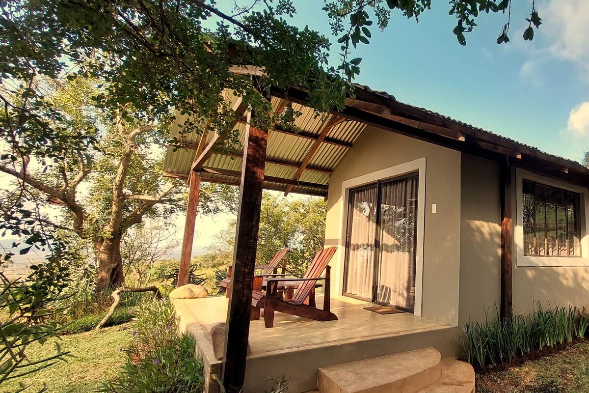 Ein Haus mit überdachter Veranda, kleiner Terrasse und Garten mit verschiedenen Pflanzen und Bäumen.