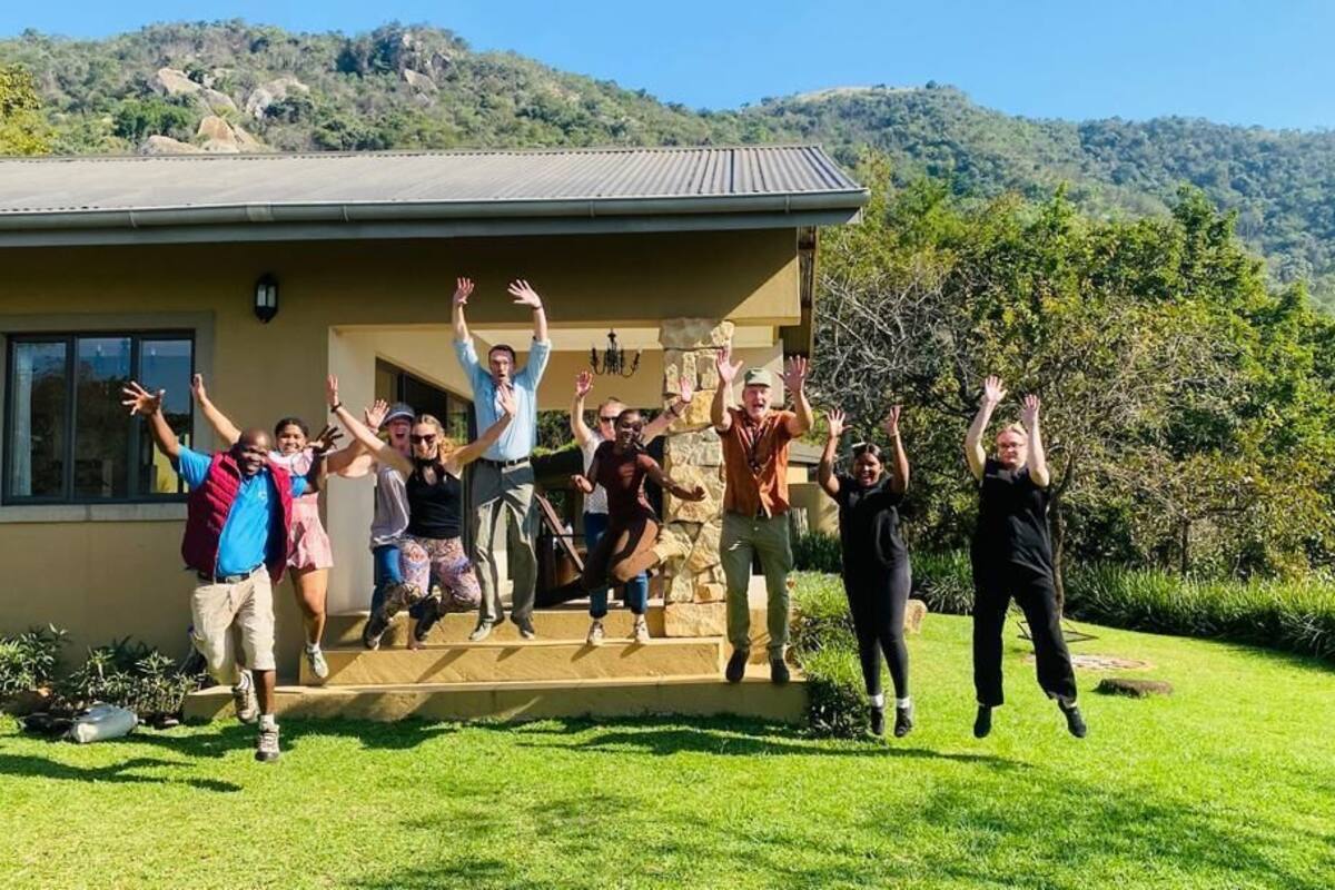 Eine Gruppe von Menschen feiert vor einem Haus mit einer Stein-Fassade und einem Rasen.