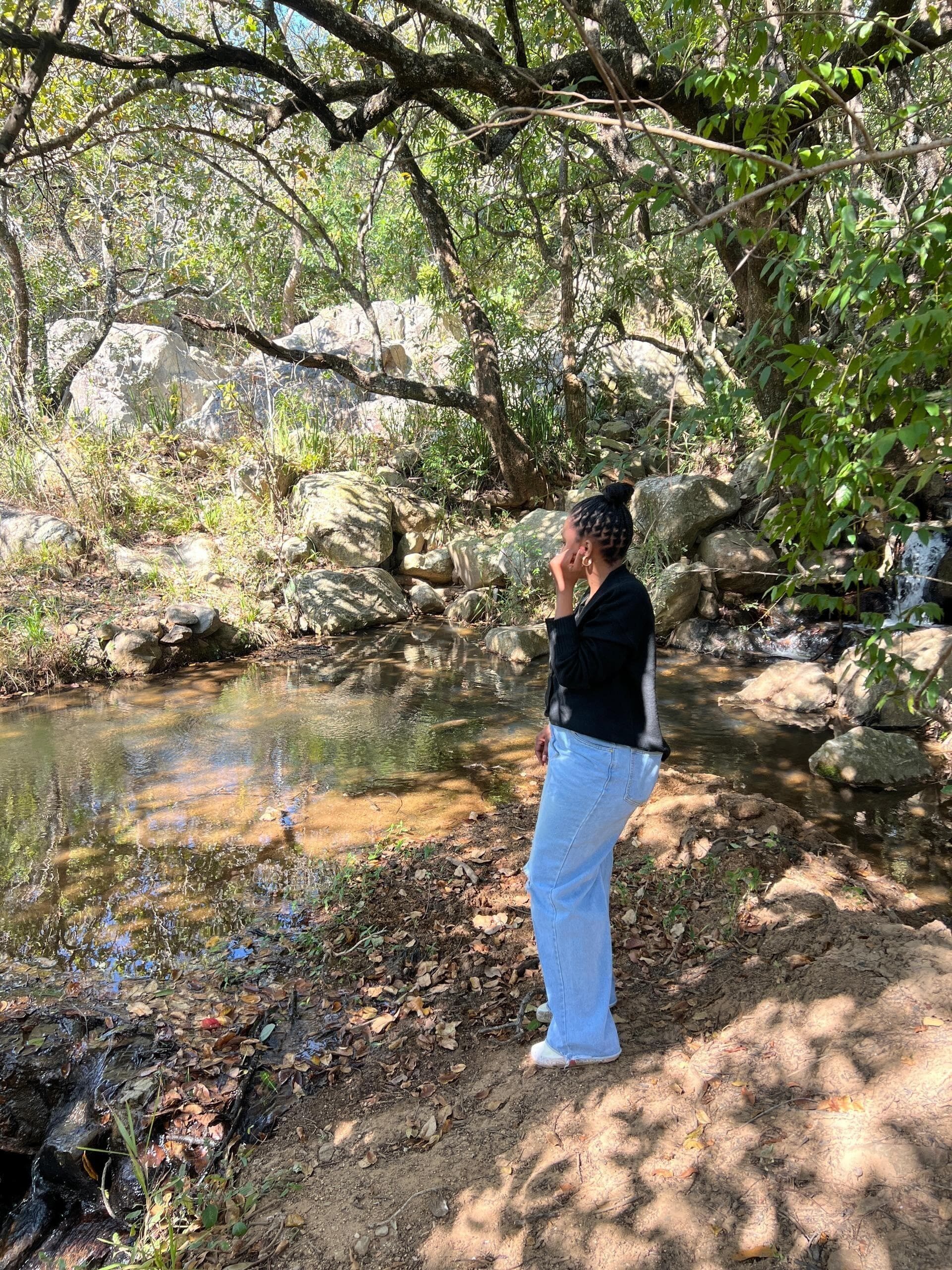 A person standing by a clear stream surrounded by rocks and greenery.