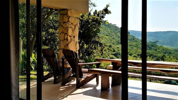 An outdoor patio with a stone pillar, wooden benches, and a view of a lush green landscape.