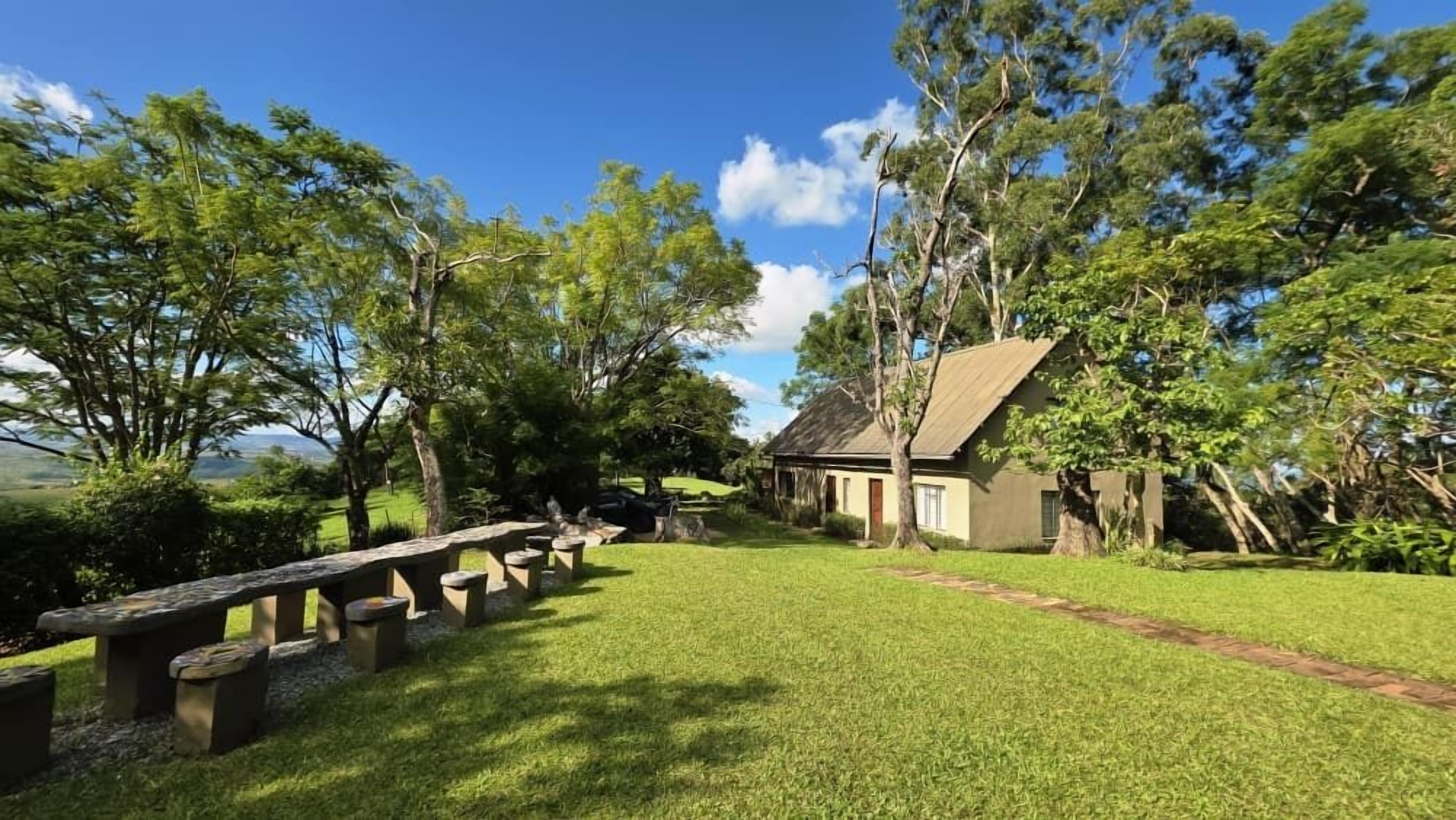 Un área con césped, una mesa de picnic, un edificio pequeño y árboles.