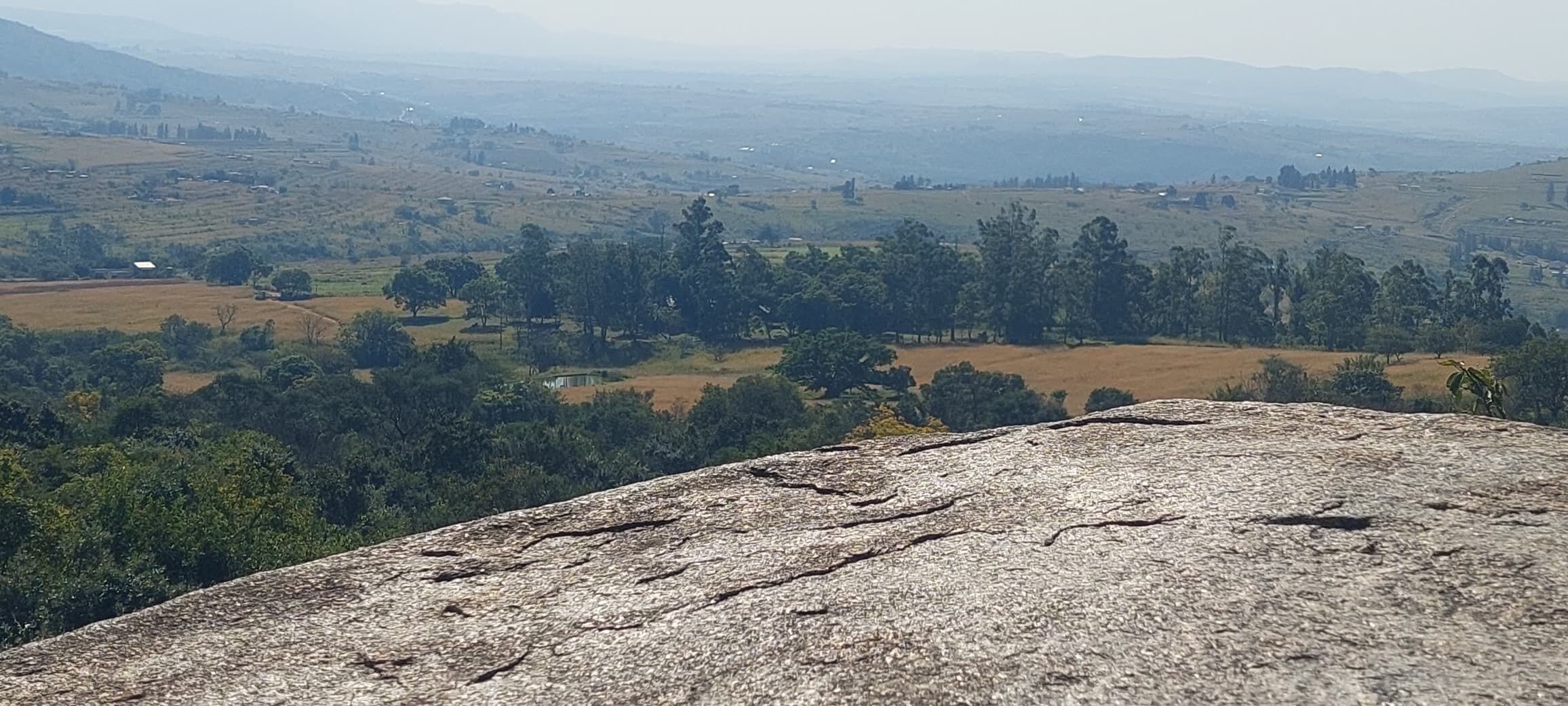 A rocky outcrop overlooking a rural landscape with fields and scattered trees.