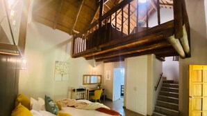 Quarto com cama, escrivaninha, cadeira e escada para outro cômodo.
