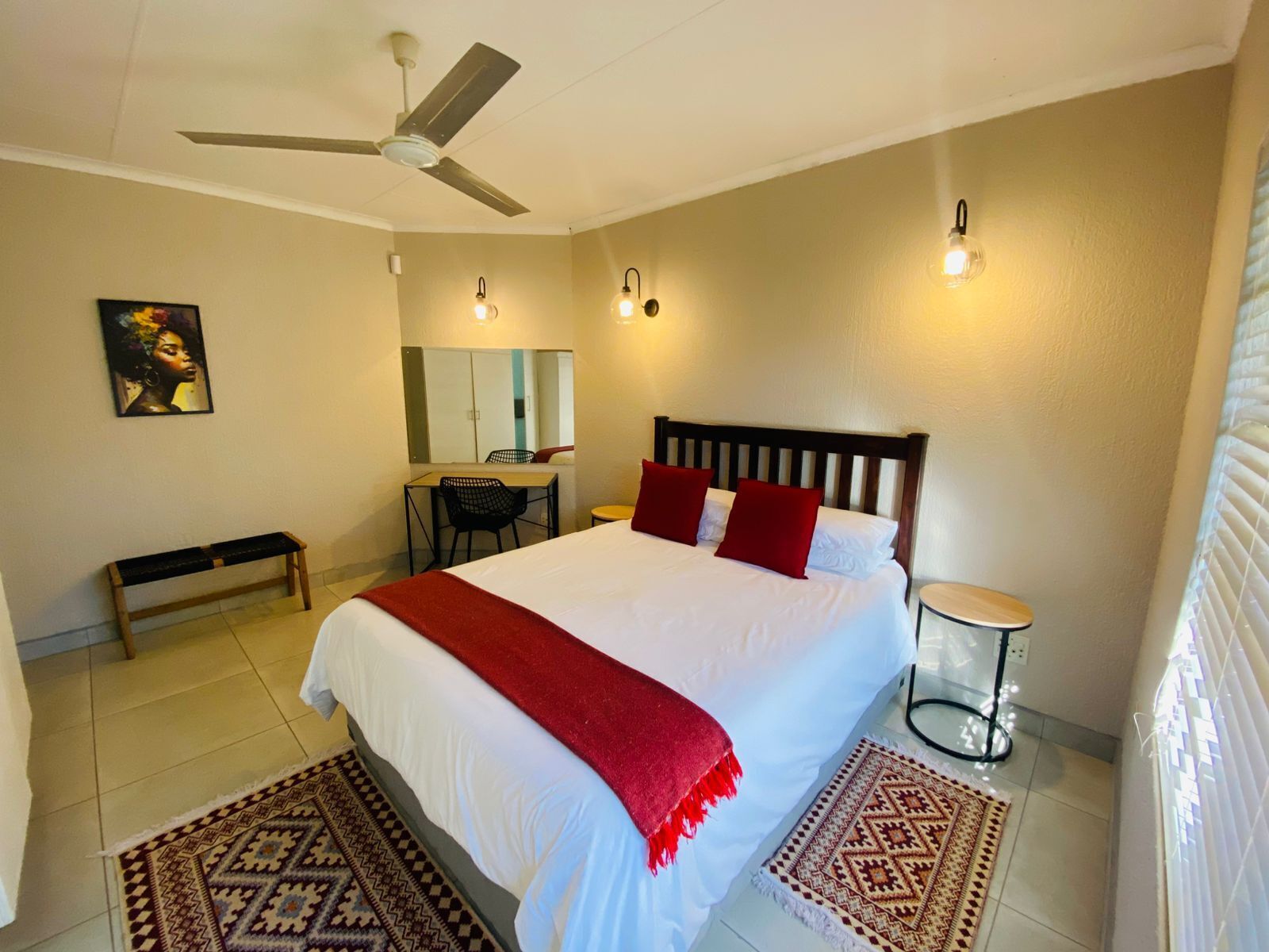 A bedroom with a bed, a desk, a chair, a bench, a round table, and a ceiling fan.