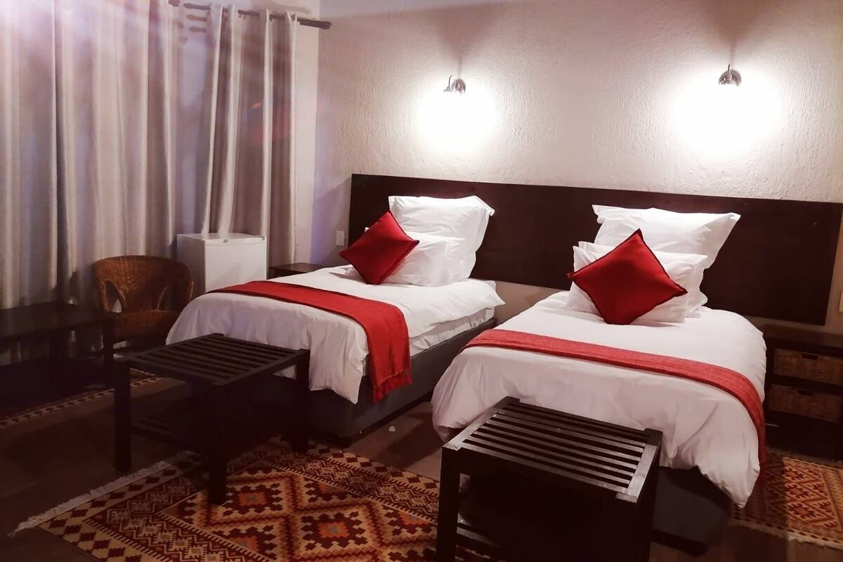 A hotel room with two beds, each with white bedding and red pillows, a patterned rug, a small table, and a chair.