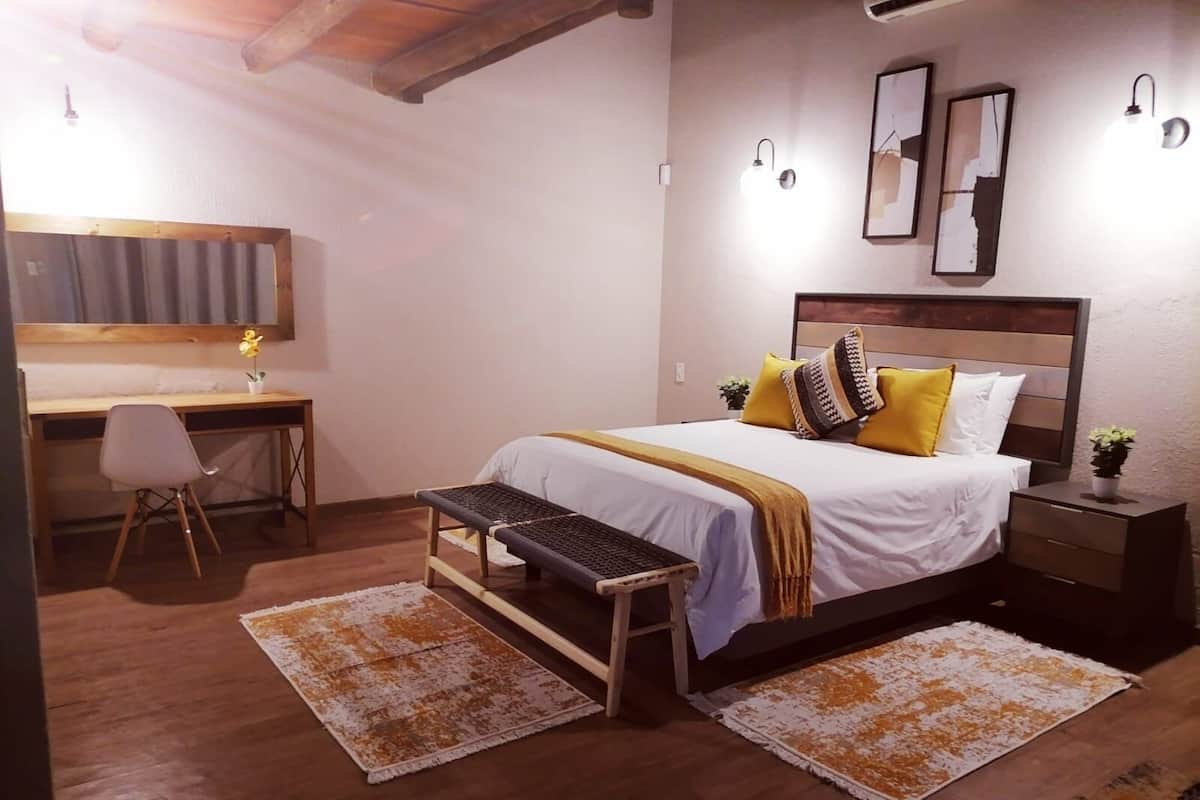 A bedroom with a bed, desk, chair, and two rugs.