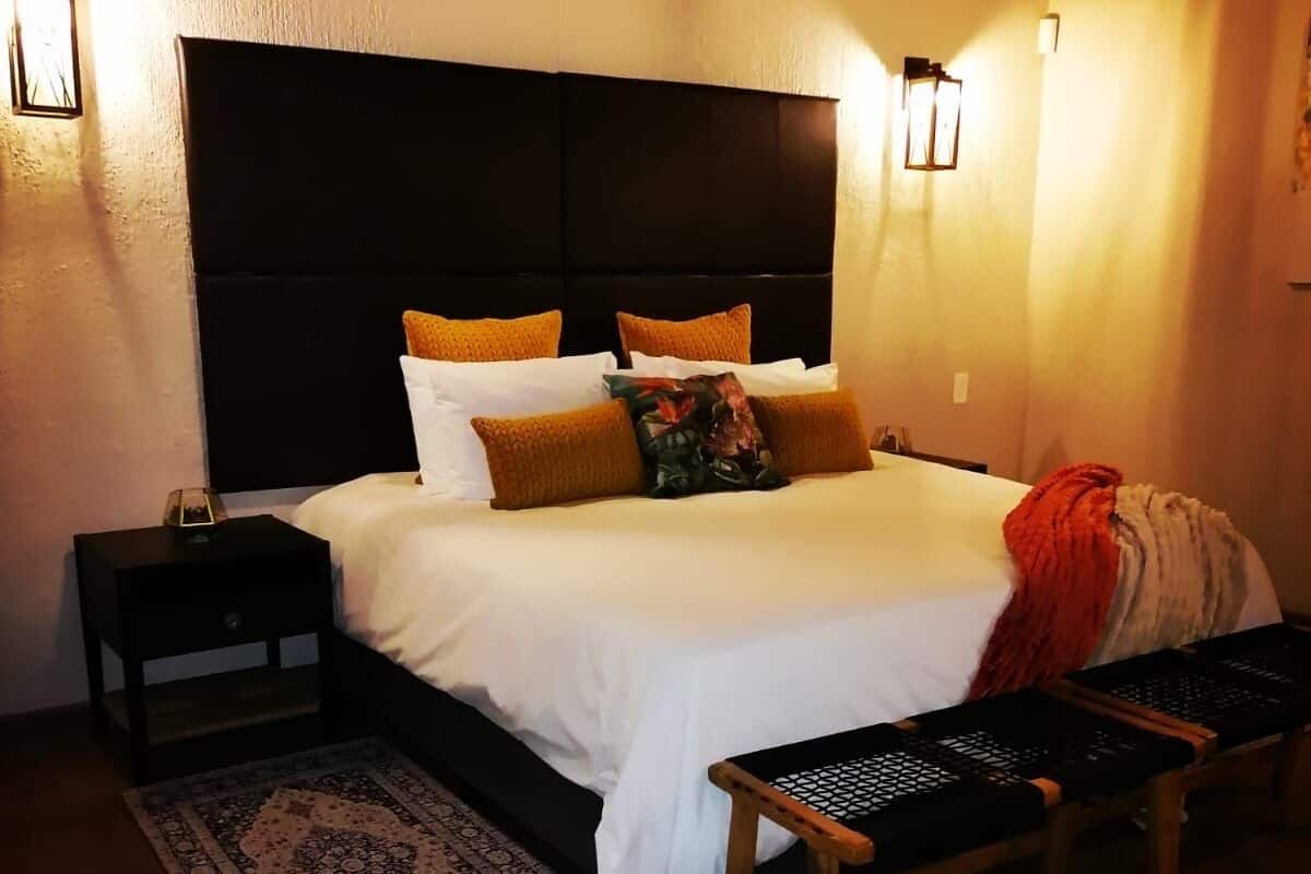 A bedroom with a large bed, two bedside tables, a bench, and patterned rugs.