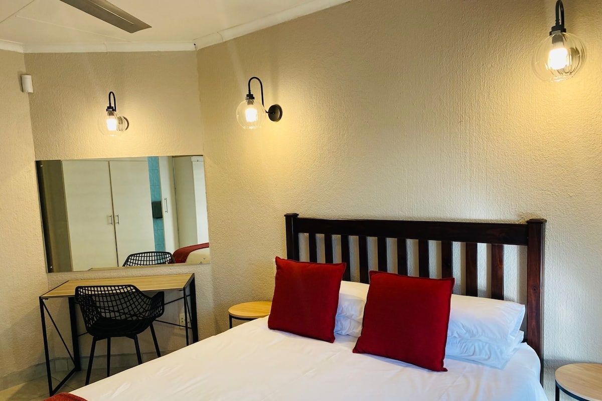 A hotel room with a bed, a desk, a chair, and two wall-mounted lights.