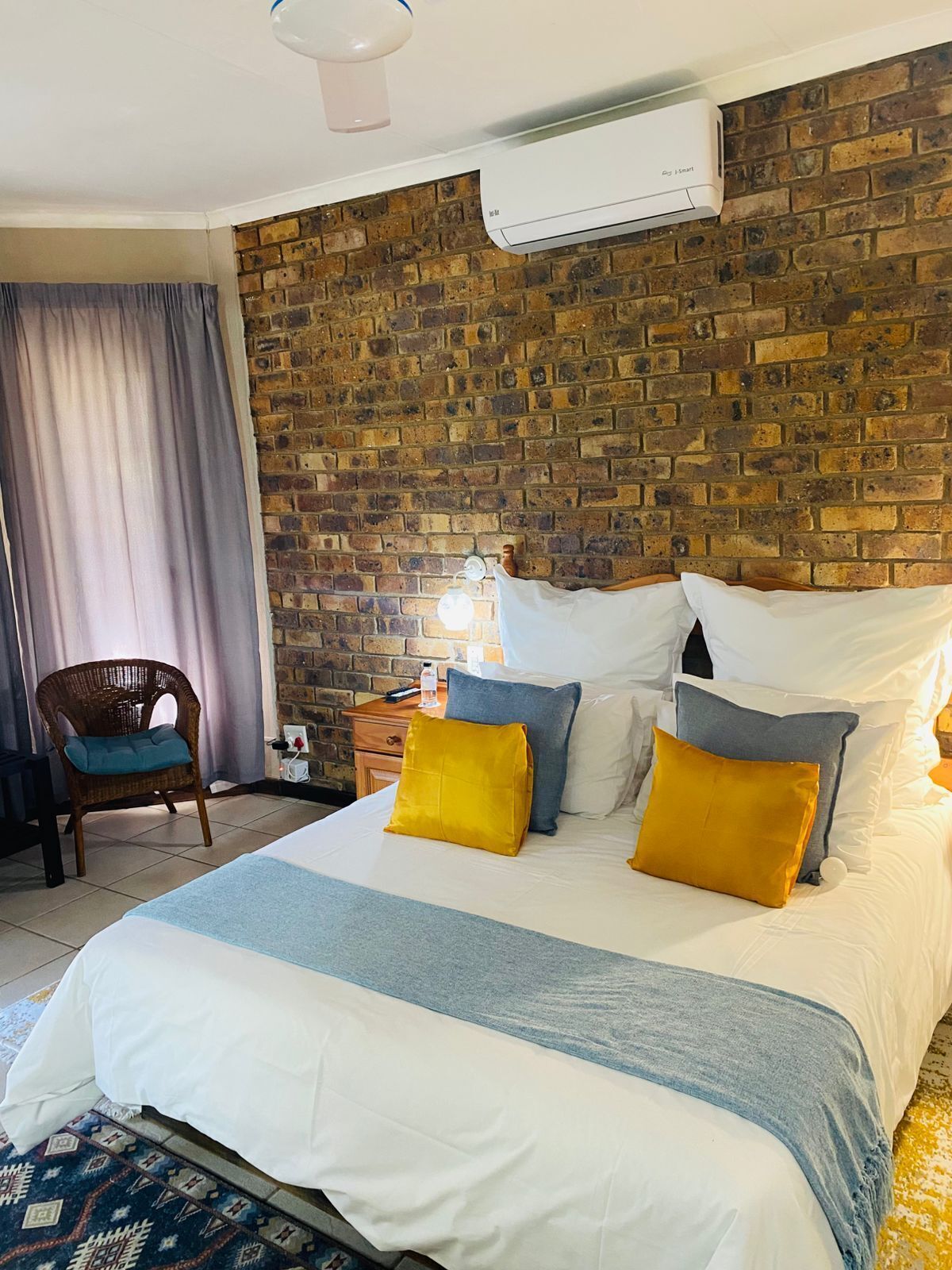 Une chambre d’hôtel avec un mur en briques, un lit avec une literie blanche et bleue, et une chaise en osier.