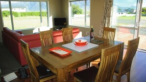 A dining area with a wooden table, red sofa, and chairs. - Spacious Quiet | 3BR | Decks | Wi-Fi | BBQ | Views (Kaikoura Township)