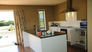 A modern kitchen with a central island, white cabinetry, and a large window offering a view of the outdoors. - Spacious Quiet | 3BR | Decks | Wi-Fi | BBQ | Views (Kaikoura Township)
