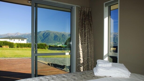 A bedroom with a bed, a view of mountains, and a wooden deck outside. - Spacious Quiet | 3BR | Decks | Wi-Fi | BBQ | Views (Kaikoura Township)