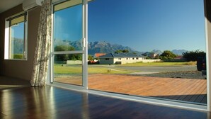 A spacious room with large windows offering a view of a mountainous landscape and a parking area. - Spacious Quiet | 3BR | Decks | Wi-Fi | BBQ | Views (Kaikoura Township)