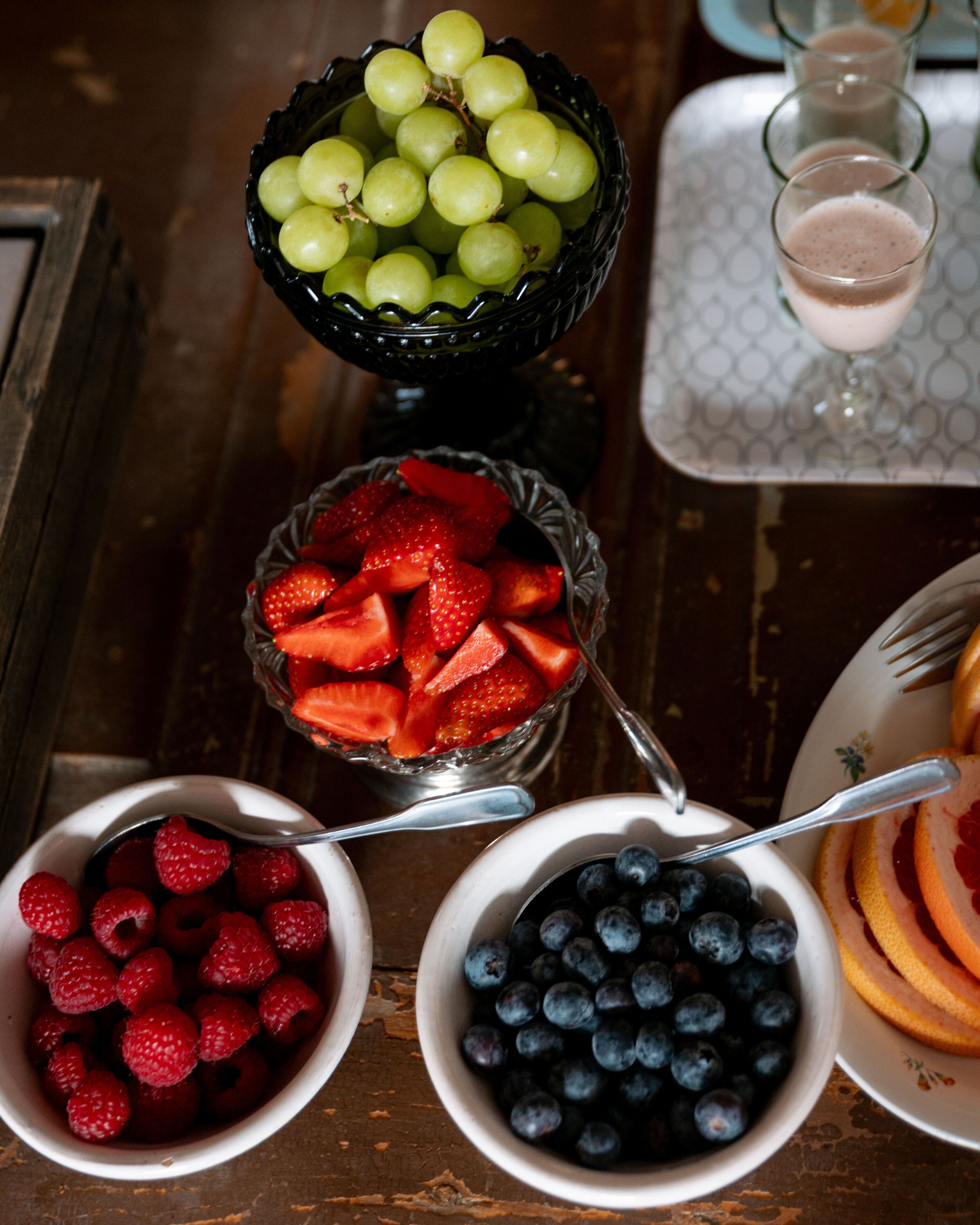 Ein Tisch mit Schalen voller frischer Früchte, darunter Trauben, Erdbeeren, Himbeeren und Blaubeeren.