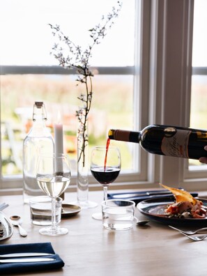 A dining table with wine glasses, a bottle of wine being poured, and a candle.