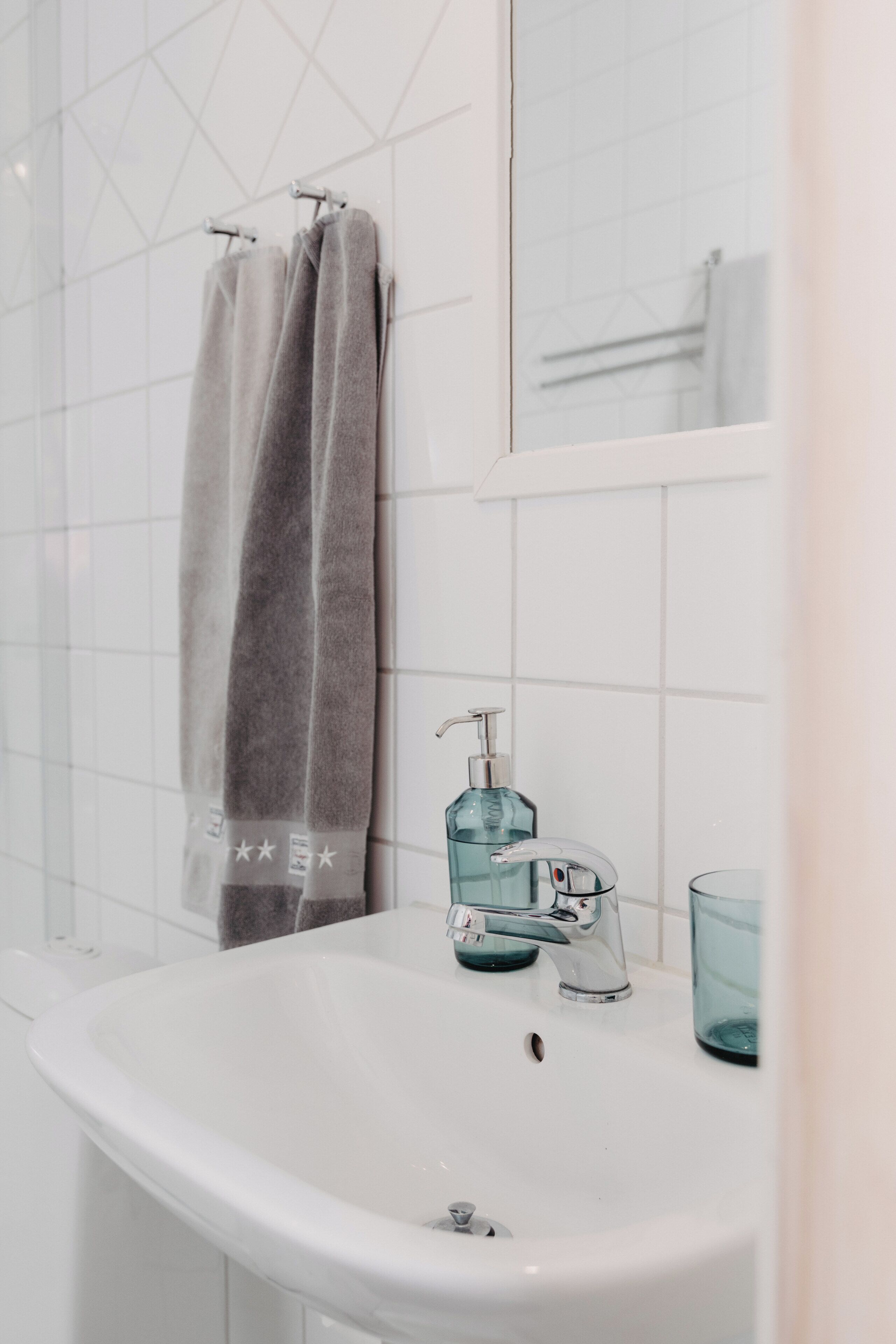Un baño con un lavabo blanco, un espejo y una toalla colgada en un perchero.
