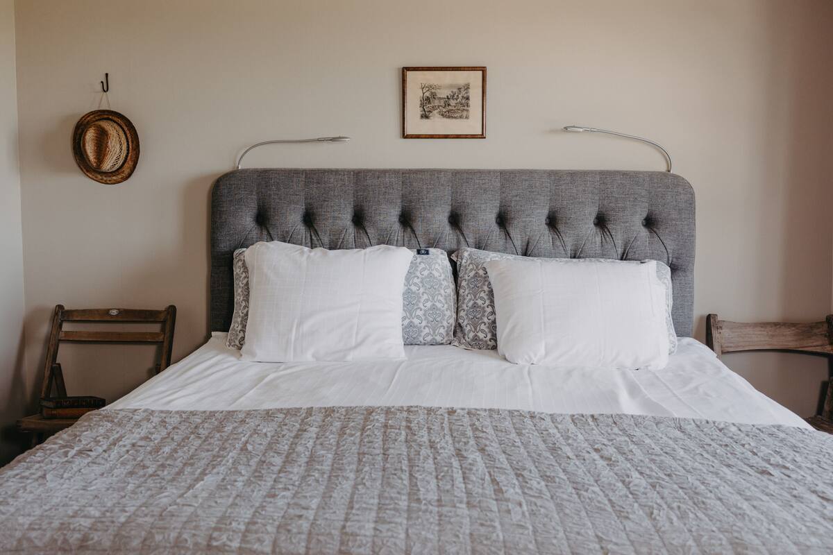 A neatly made bed with a grey upholstered headboard, white linens, and patterned pillows.