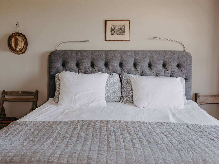 Una cama bien hecha con un cabecero tapizado en gris, sábanas blancas y almohadas estampadas.