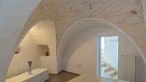 Et soveværelse med en stor seng, et toiletbord med en vase, og en trappe til en etage ovenover.
