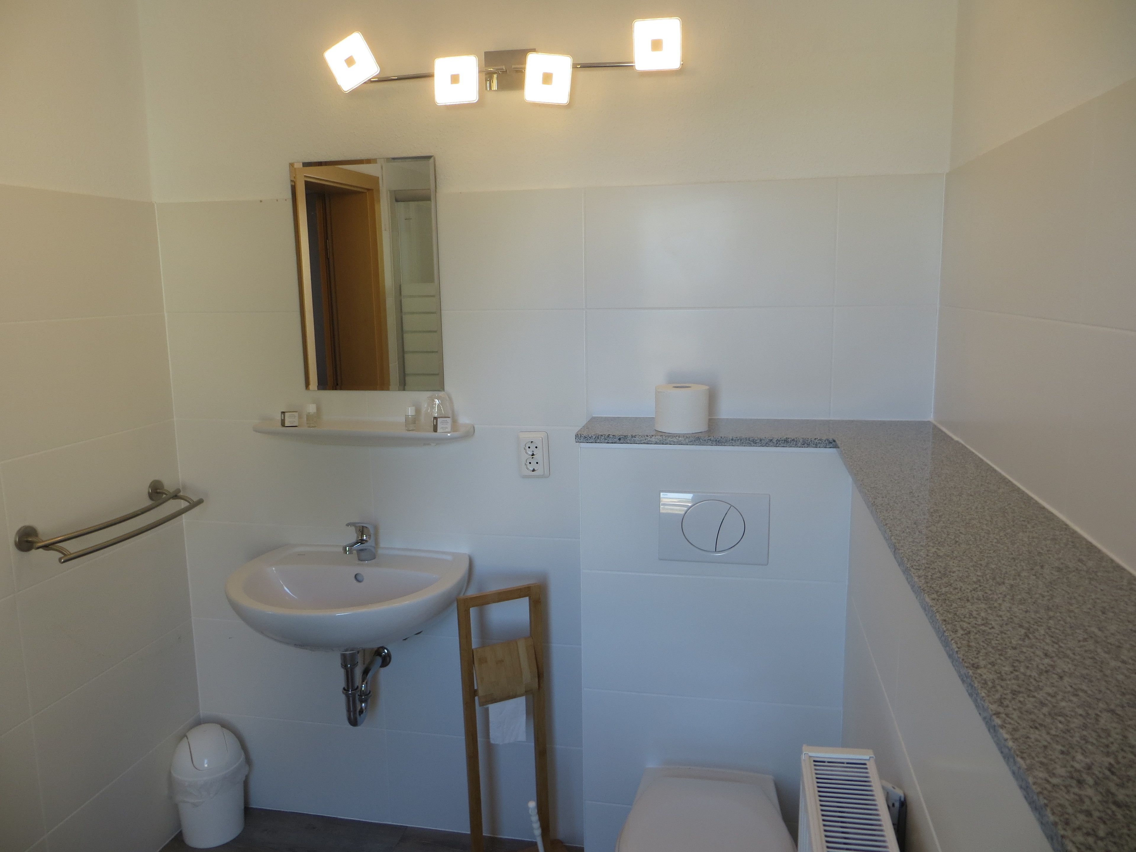 A bathroom with a sink, mirror, towel rack, toilet, and a ventilation unit.