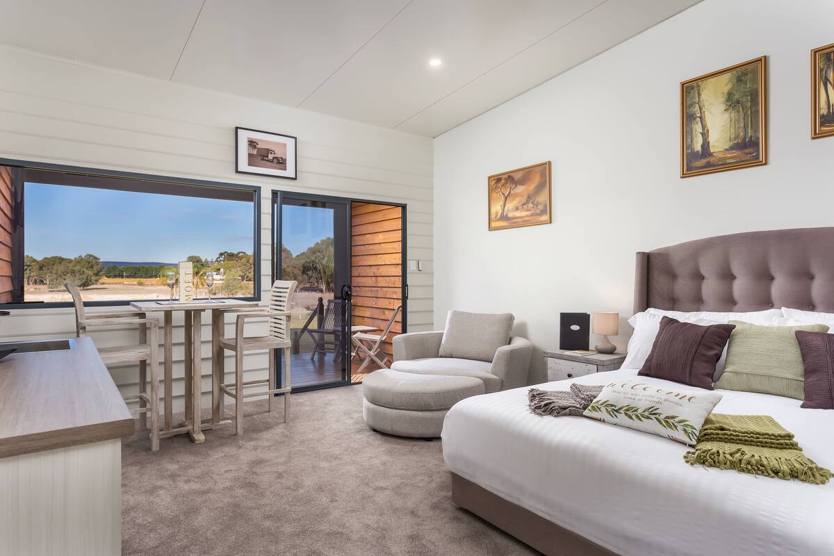 A bedroom with a large bed, a desk, and a chair. There is a window with a view of the outdoors.