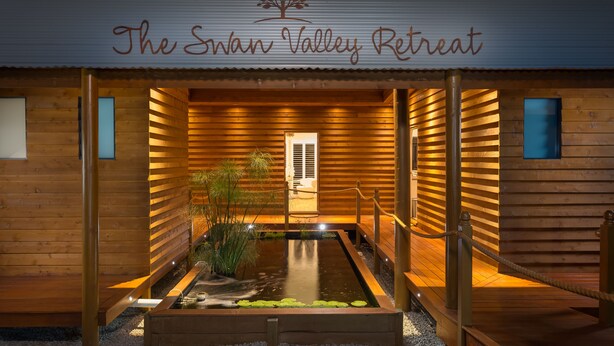 Swan Valley Retreat, com fachada de madeira, um pequeno lago e uma placa sobre a entrada.