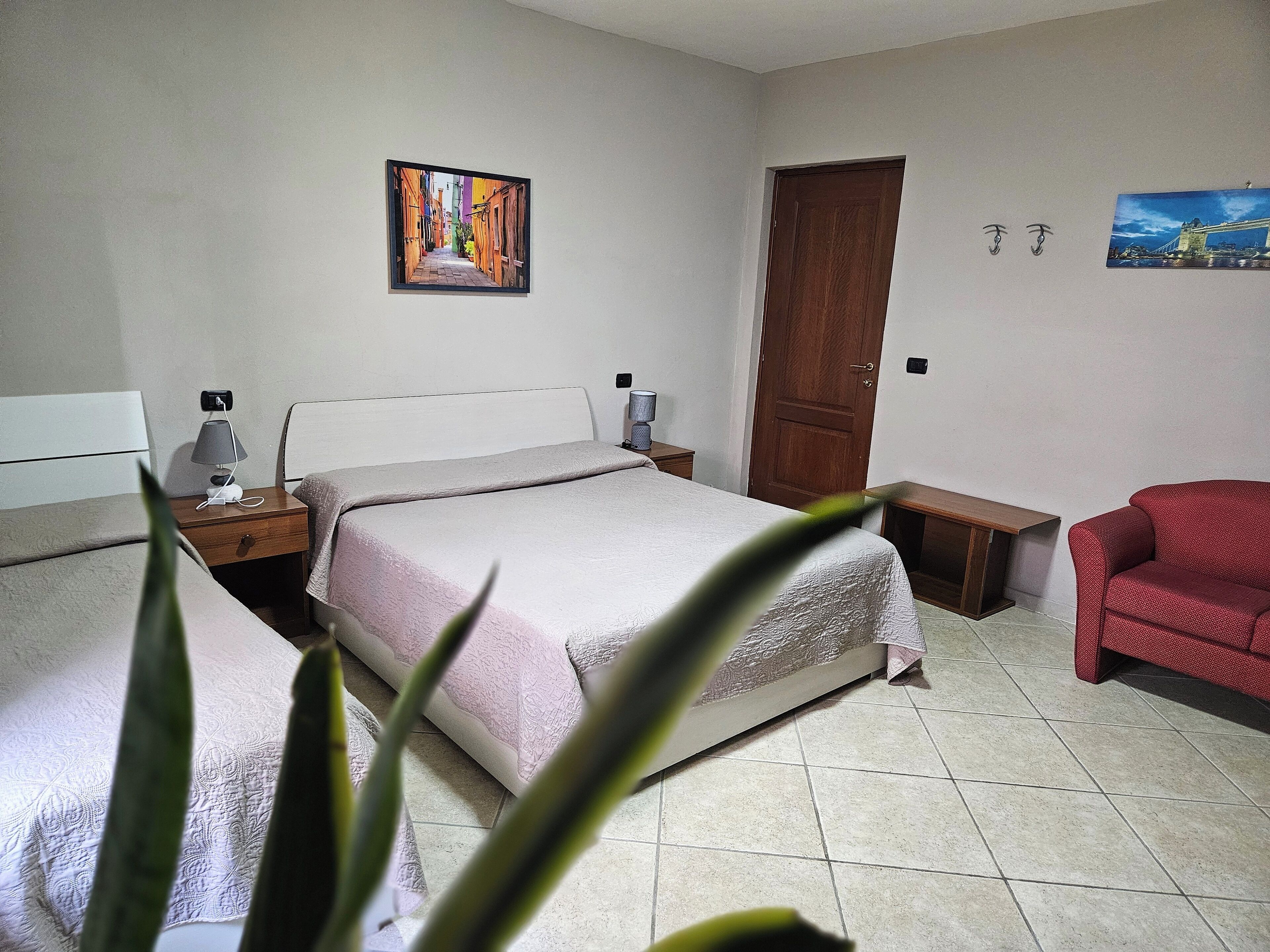 A bedroom with a bed, bedside tables, a chair, a door, and two wall-mounted pictures.