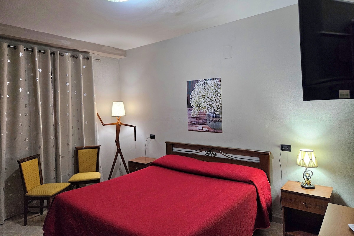 A hotel room with a bed, a desk, a chair, a lamp, and a painting on the wall.